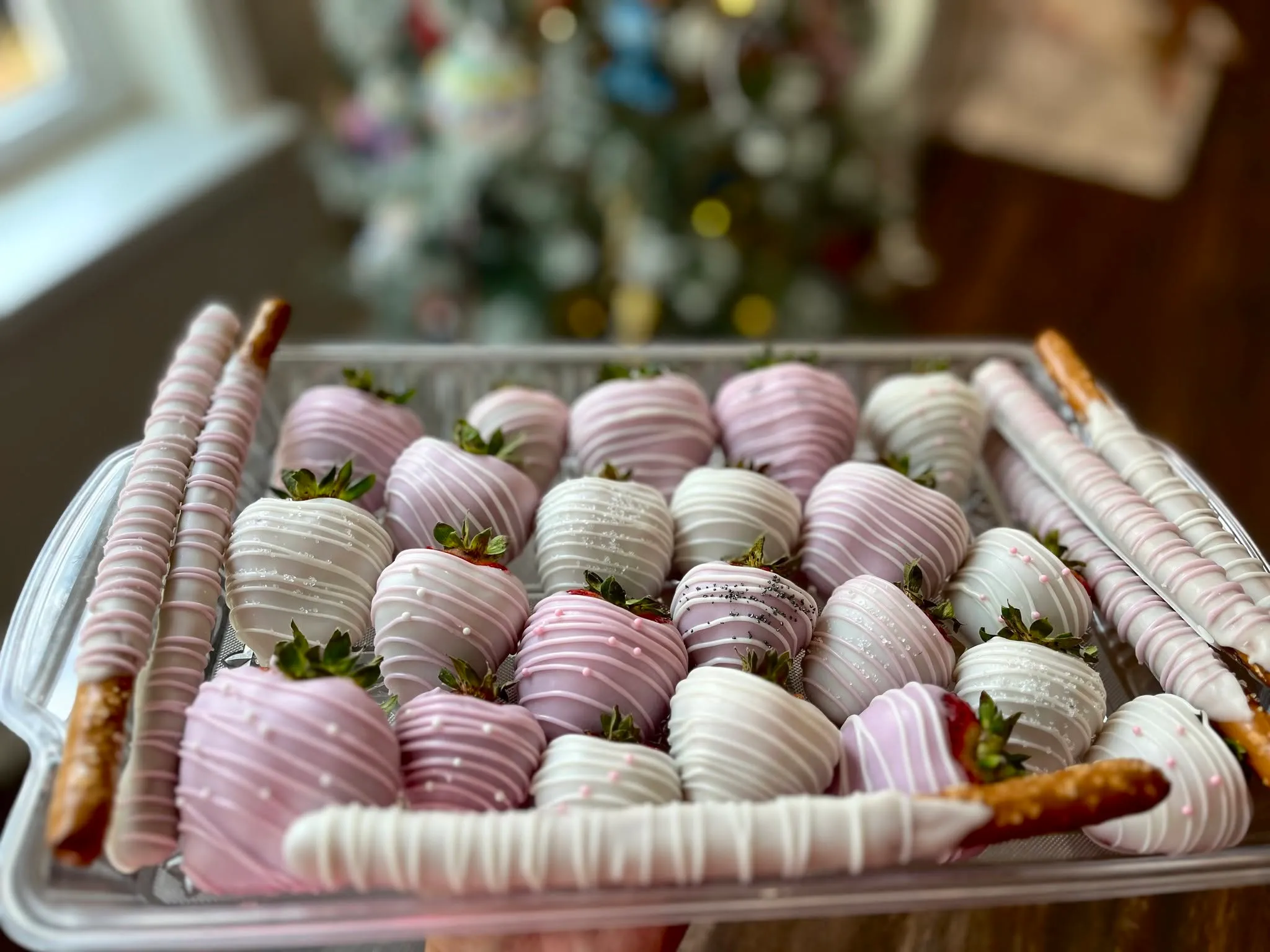 A tray of chocolate-dipped strawberries and pretzel rods, drizzled in pink and white