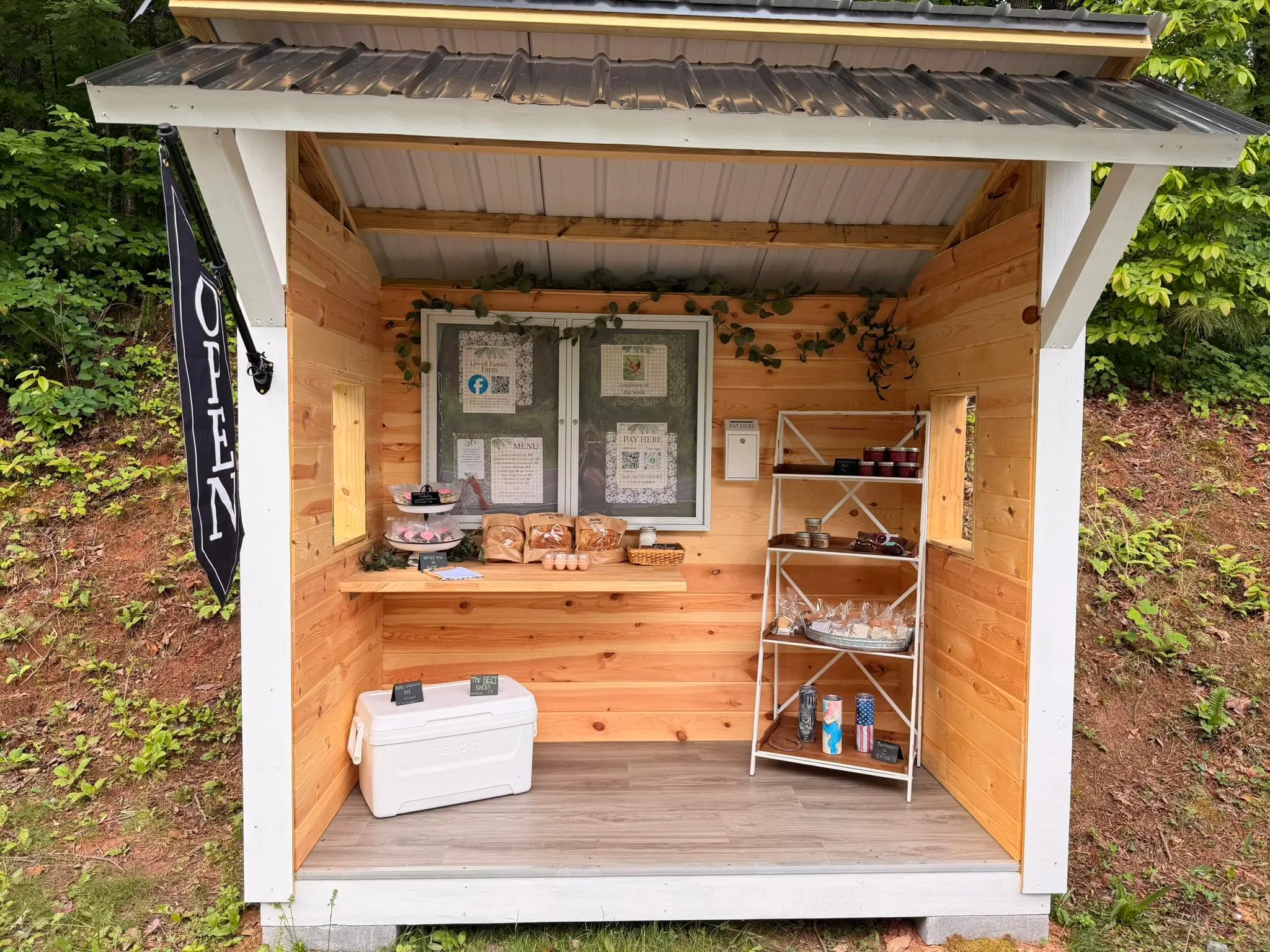 The Lovell Family Farm stand, shelves stocked with bread, jarred preserves and a basket of eggs