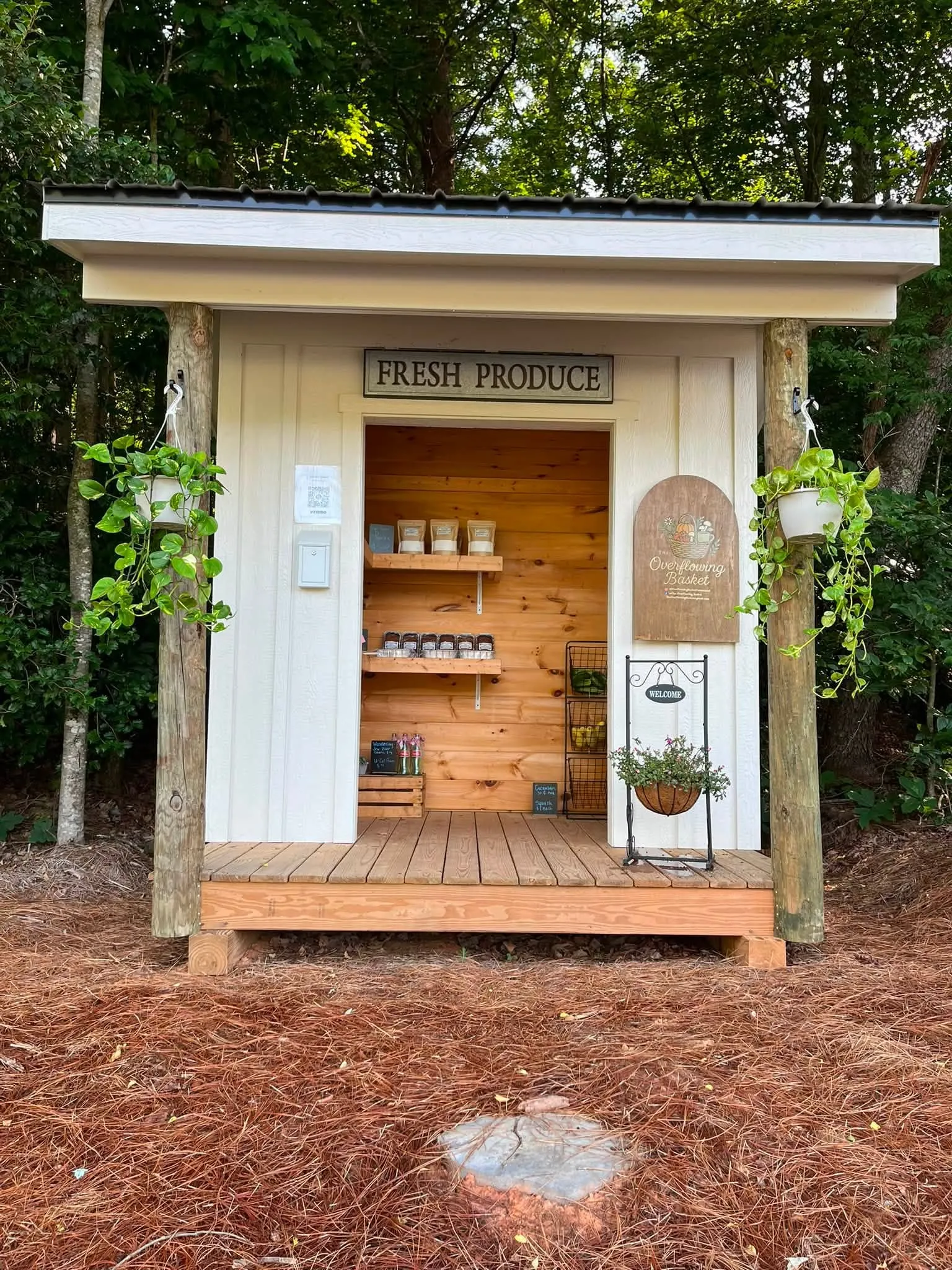 The Overflowing Basket farm stand, a small covered shed with shelves of produce and jarred goods and a sign reading Fresh Produce