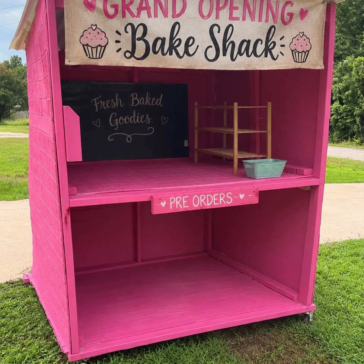 The pink Sarah's Bake Shack stand, with a Grand Opening banner and a chalkboard sign reading Fresh Baked Goodies